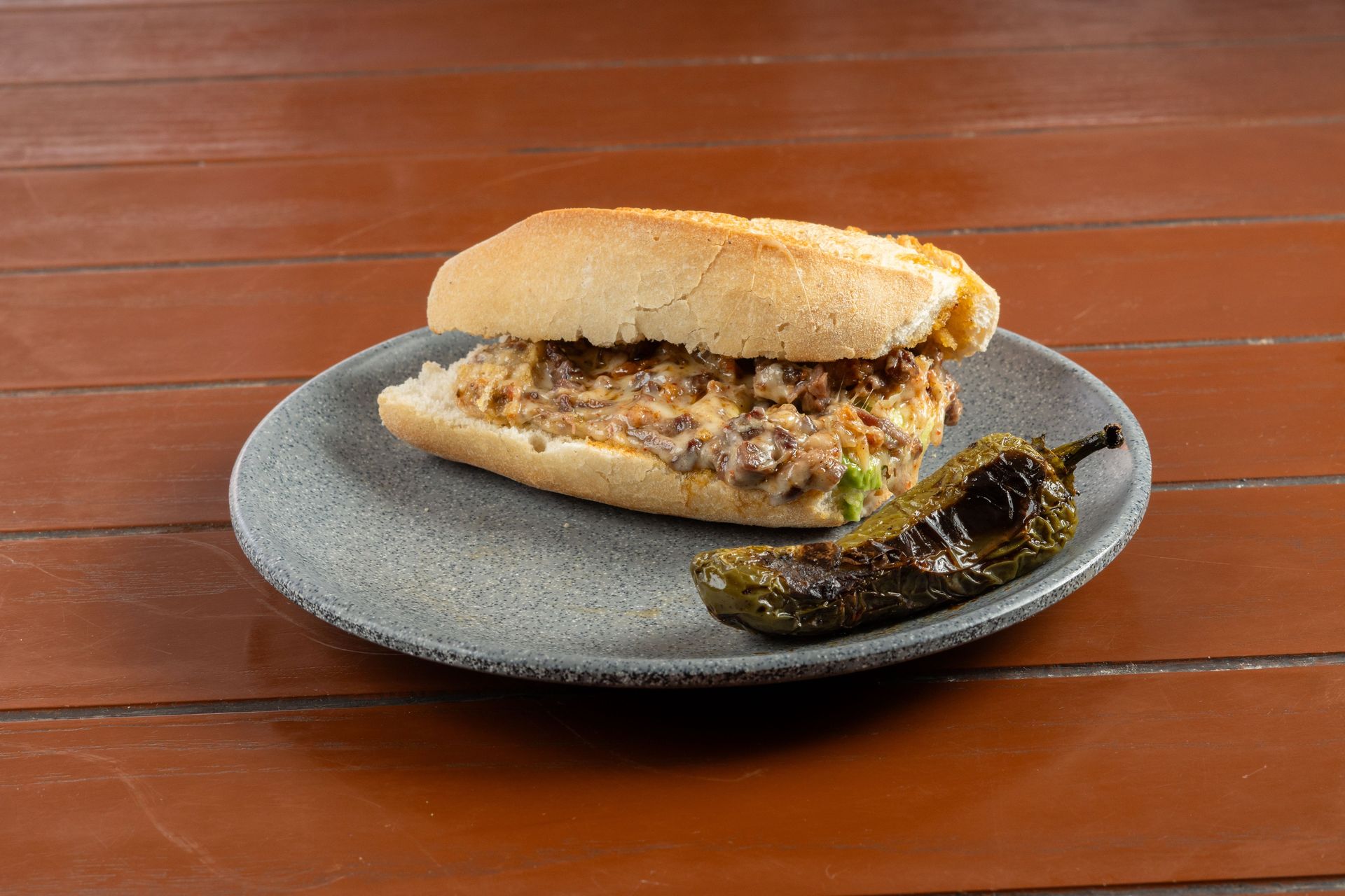 Tasty grilled sandwich filled with melted cheese and meat, served with a roasted jalapeño on a plate.